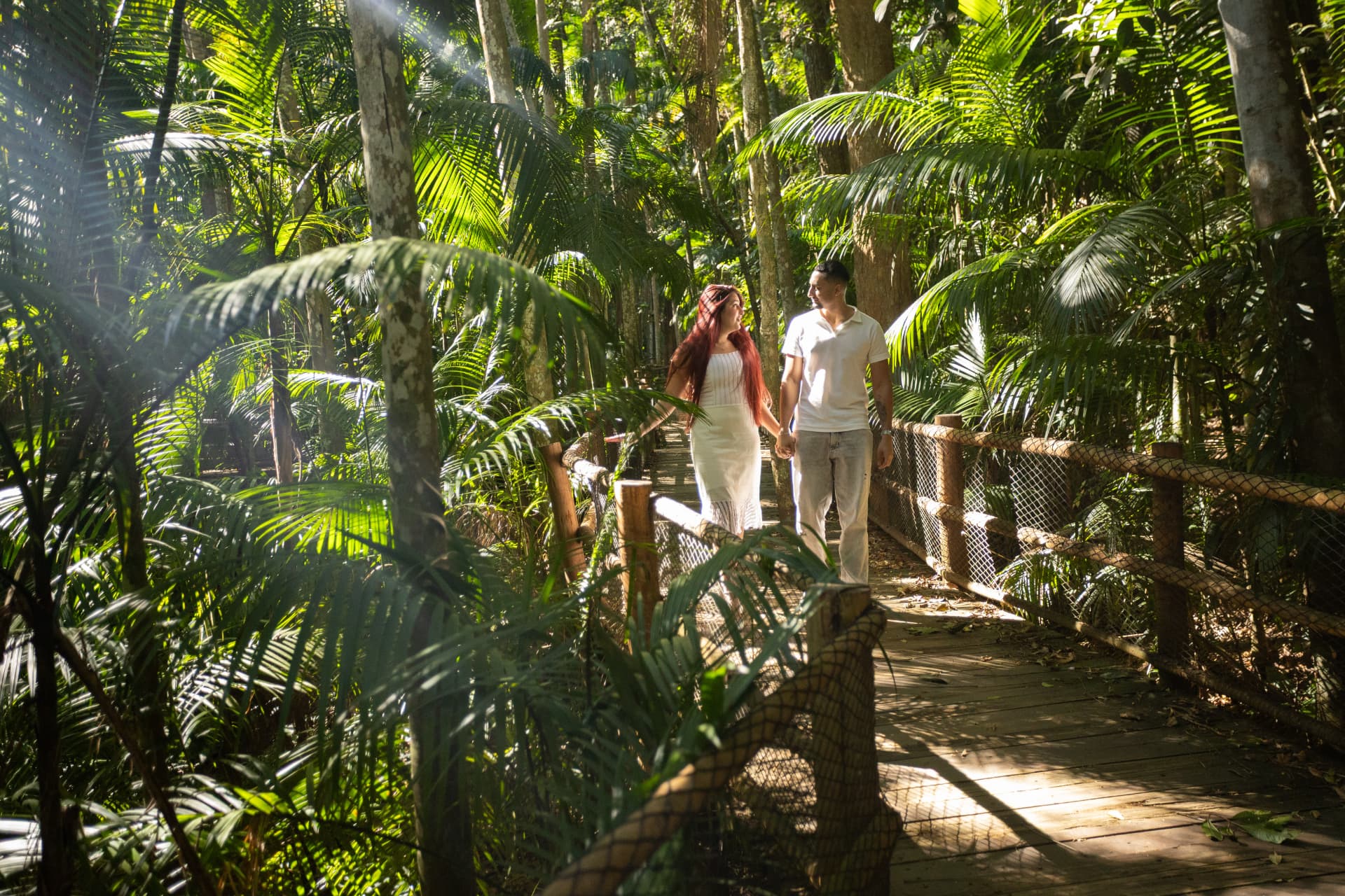 Carlos e Ketelyn caminhando de mãos dadas por uma trilha de madeira na floresta